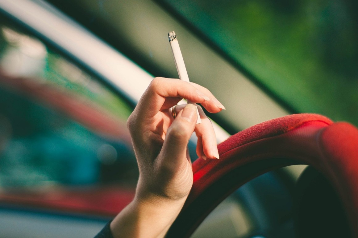 Hand on steering wheel holding cigarette