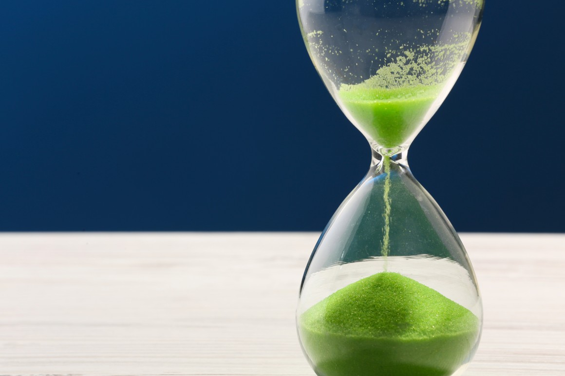 Photo of hourglass with green sand trickling through it against a blue background