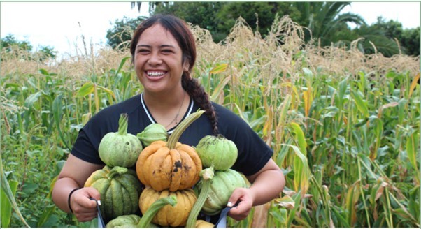 Teenage girl outside holding an arm full of small pumpkins with a big smile on her face.