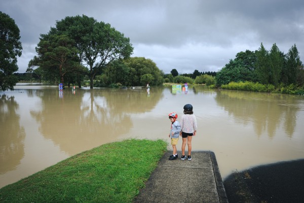 Children standing at the edge of large pool of floodwater post cyclone Gabrielle.
