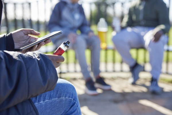 youth sitting in park with electronic cigarette / vape