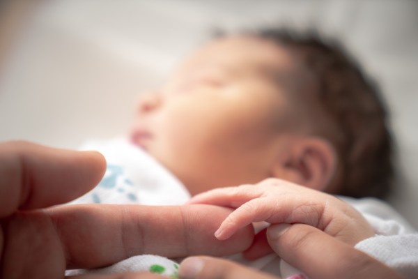 Image of sleeping newborn baby with hand on adult finger in foreground