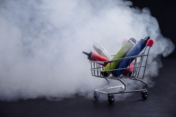 photo of disposable vapes in a small shopping cart, with cloud of smoke and black background