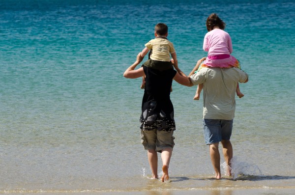 Two adults with children on shoulders, wading on beach