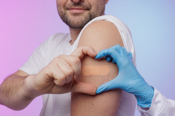 Hand forming a heart shape around band-aid on arm after vaccination. 