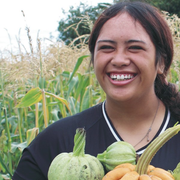 Teenage girl outside holding an arm full of small pumpkins with a big smile on her face.